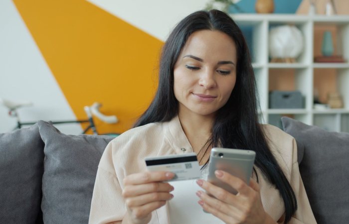 Woman sitting on sofa shopping online with mobile and credit card.