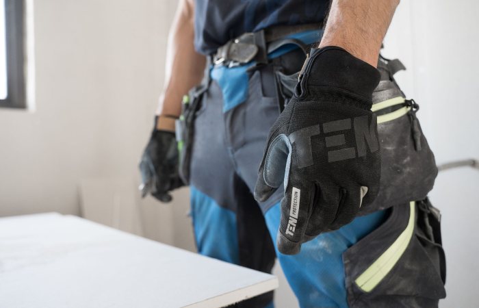 Close-up of a construction worker wearing safety gloves indoors, focused on hand protection.