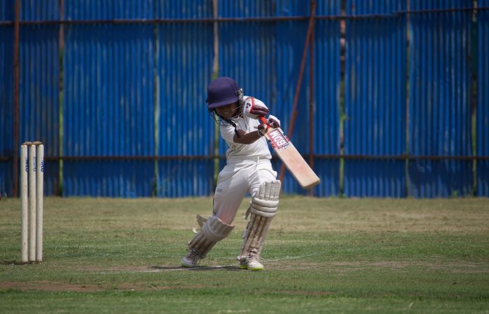 A young cricketer in action on a sunny day, playing on a grass field with a bat and wicket.