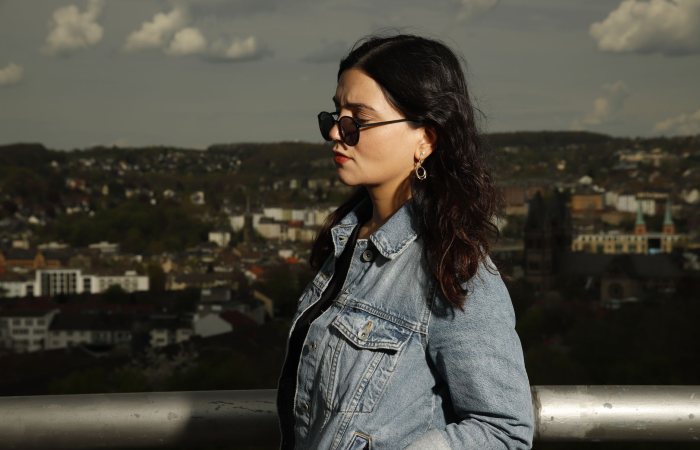 Stylish woman in denim jacket with city skyline backdrop.