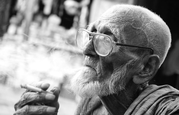 Close-up portrait of an elderly man smoking in monochrome, displaying deep character and life experience.