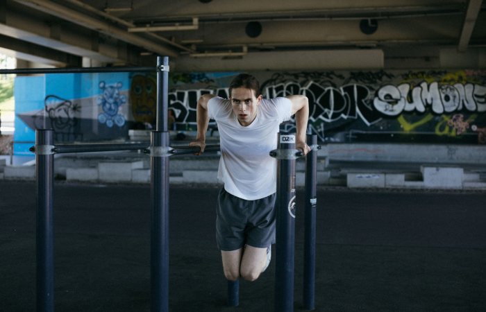 Athletic man in urban setting exercises on bars with vibrant graffiti background, showcasing flexibility.