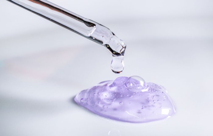Pipette releasing drop of purple gel, highlighting skincare and laboratory use.